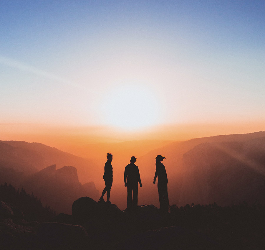 Group of three people silhouetted against sunset with blue sky and mountains